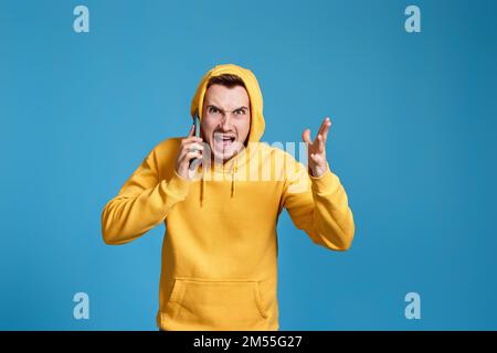 angry man in yellow sweatshirt holding mobile phone Stock Photo