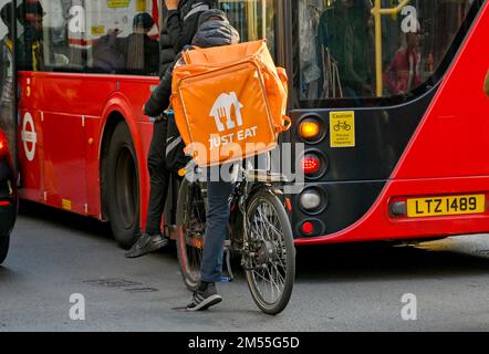London, England, UK - June 2022: Delivery person for Just Eat on a bicycle waiting behind a red London bus on a street in central London Stock Photo