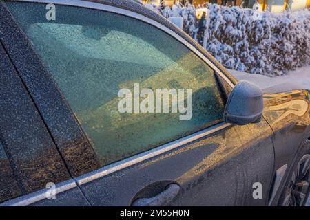 Close up view of snow-covered side door of car with folding mirror in parking lot on frosty winter day. Sweden. Stock Photo