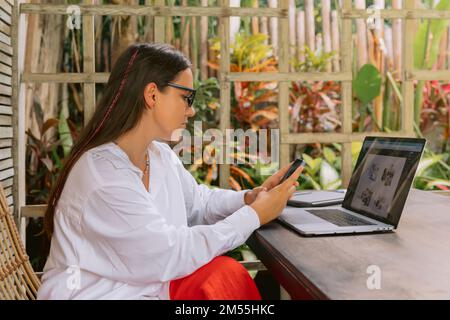 Attractive young woman using smartphone and laptop computer in summer office Stock Photo