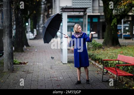 A woman with an umbrella is the street checking for rain. Stock Photo