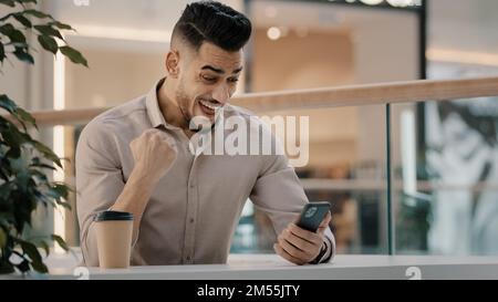 Indian Hispanic man happy shocked amazed male businessman has offer online message good news excited winner guy win victory financial prize with Stock Photo