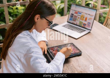 Attractive young woman designer using digital tablet and laptop computer in summer office Stock Photo