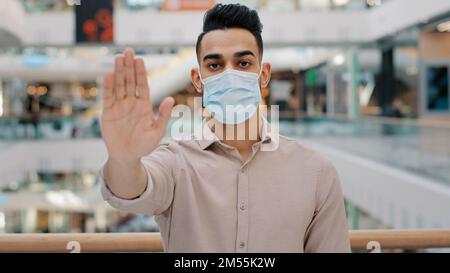 Portrait of young hispanic man wearing medical mask put palm forward serious ethnic guy looking at camera male showing stop sign palm with hand Stock Photo