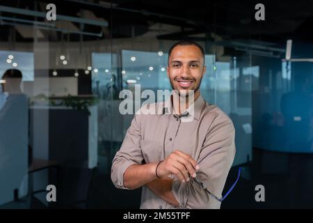 Portrait of african american businessman in office, man in shirt standing near window smiling and looking at camera, programmer working inside development company. Stock Photo