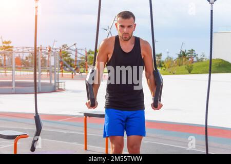Young man stands on his hands hanging on the gymnastic rings on the city sports ground Stock Photo
