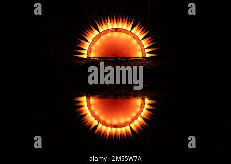 Artificial fantastic sun with sun rays or flames rising or setting reflecting in the water with a black background Stock Photo