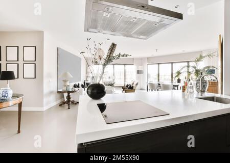 a modern kitchen with white counter tops and black appliances in the center of the photo is an open living room Stock Photo