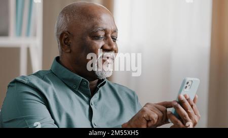 Close up bald American bearded old senior man with gray beard elderly male using software application net on cellphone reading message email swiping Stock Photo