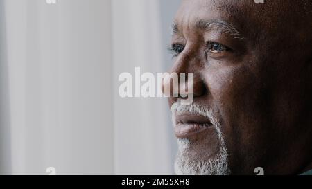 Close up pensive male old wrinkled face, 60s African bearded man deep in sad thoughts looking at window, elderly grandfather look away think about Stock Photo