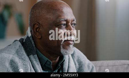 Unhealthy mature elderly grandpa looking away in window pensive sick African American man suffering flu respiratory virus ill male covered in blanket Stock Photo