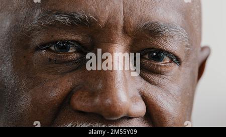 Macro extreme close up half part of face elderly middle-aged African old wrinkled man with dark eyes sad calm mature male senior citizen looking at Stock Photo