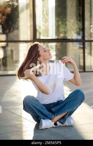 Middle age woman sitting on floor in urban city,wearing casual clothes, happienes concept, sunset light Stock Photo