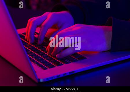 A man uses a laptop, close-up, male hands in neon lighting. Stock Photo