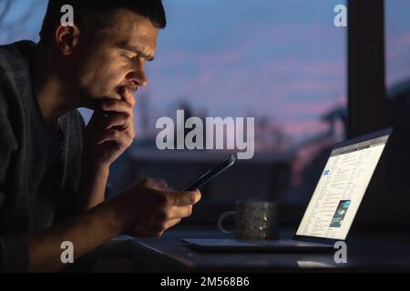 A man works on a laptop early in the morning at dawn in the dark. Stock Photo