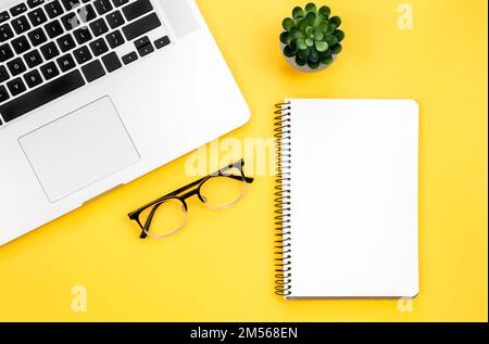 Laptop, glasses and blank notepad on yellow background, flat lay. Stock Photo