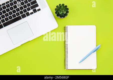 Laptop and blank notepad on green background, flat lay. Stock Photo