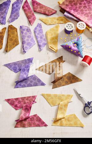 Stacks of multi-colored pieces of fabric, pieces of fabric sewn in the shape of the letter Z, pincushion, sewing accessories on a white surface Stock Photo