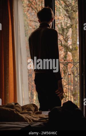 Young handsome man looking out his window at home in the room alone ...
