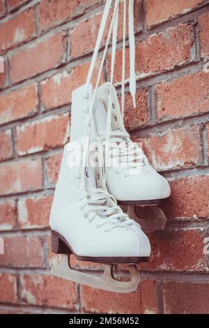 White figure skating skates hang on a brick wall in a barn Stock Photo