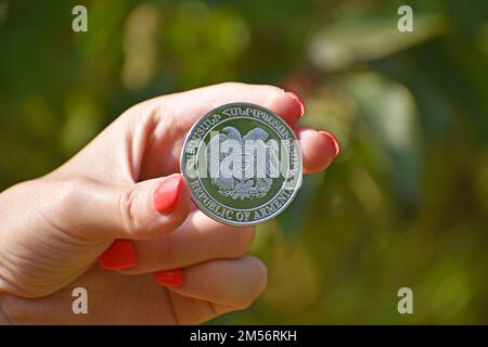 A close up of a woman's hand holding a coin with the Coat of arms of Armenia on it, blurred background Stock Photo