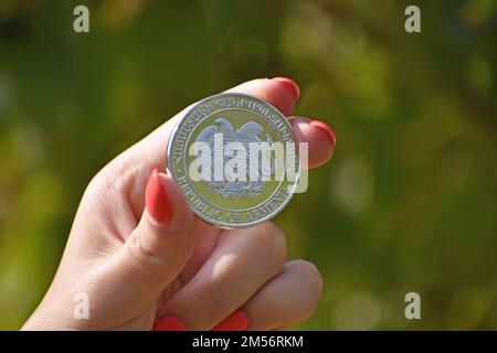 A close up of a woman's hand holding a coin with the Coat of arms of Armenia on it, blurred background Stock Photo