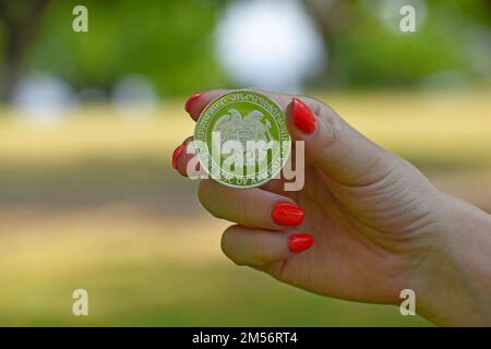 A close up of a woman's hand holding a coin with the Coat of arms of Armenia on it, blurred background Stock Photo