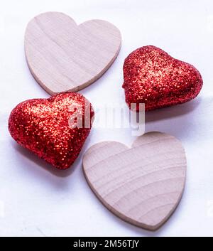 Two red glitter hearts with two plain wooden hearts together on a white background Stock Photo