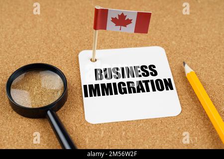 On the table is the flag of Canada, a pencil, a magnifying glass and a sheet of paper with the inscription - Business immigration Stock Photo