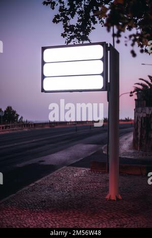 A vertical selective focus capture of three empty white color street sign templates by the roadside of the sidewalk with the purple dusk sunset in the Stock Photo