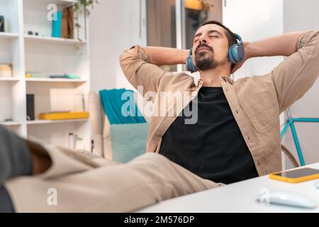 Relaxed worker sitting with his feet on the table at home in the workplace with headphones Stock Photo