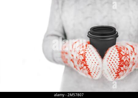 Woman drinking hot coffee from paper cup. Concept of frost winter season.Girl in yarn mittens holding black mug in her hands over white background. Ph Stock Photo