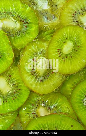 Close-up fresh slices of juicy kiwi fruit on white background. Slices of kiwi fruit in sparkling water on white background, closeup. Vertical image Stock Photo