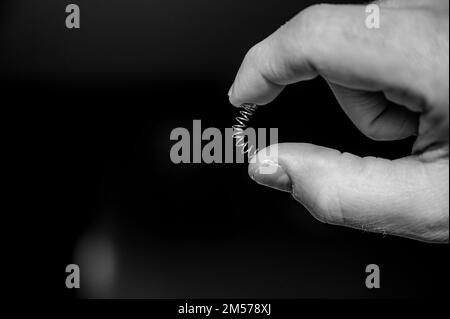 Caucasian hand compressing a metal spring between a thumb and finger ...