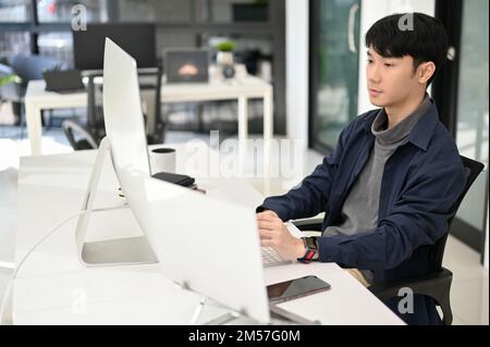 Professional and smart young Asian male web developer working at his modern office desk, using pc computer and laptop computer to create his website. Stock Photo