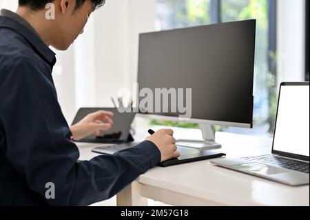 Focused and smart young Asian male programmer or web developer working at his office desk, designing his new website project. Stock Photo
