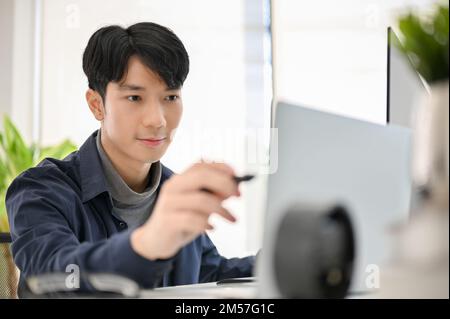 Smart and determined young Asian male programmer or web developer working at his office desk. Stock Photo