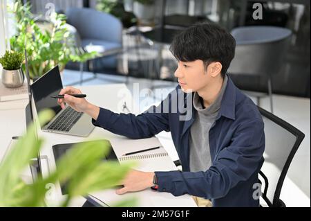 Smart and professional young Asian male programmer or web developer working at his office desk. side view Stock Photo