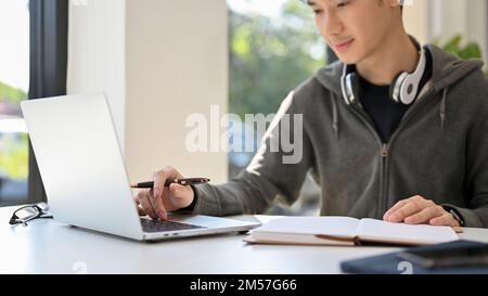 Good looking young Asian male office worker working at his desk, managing his business tasks, using laptop computer. cropped image Stock Photo