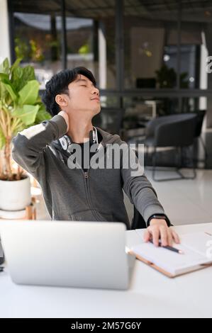 Portrait, Handsome young Asian male office worker, stretching his neck, relaxing after work at his desk. Stock Photo