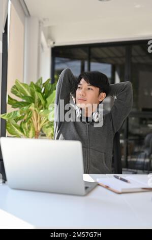 Portrait, Happy young Asian male office worker or college student relaxing after finish work at his desk, looking out the window, daydreaming about su Stock Photo