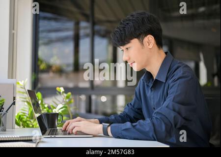 Professional young Asian businessman or male office worker using laptop computer, typing on notebook keyboard at his office desk. rear view Stock Photo