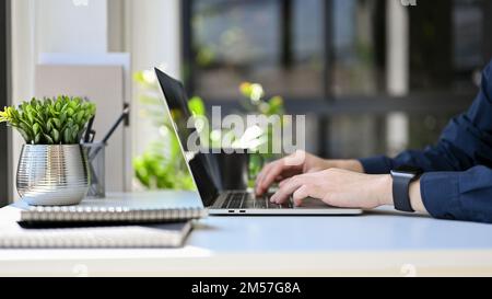 side view, cropped image, Professional businessman or male office worker using laptop computer, typing on notebook keyboard at his office desk. Stock Photo
