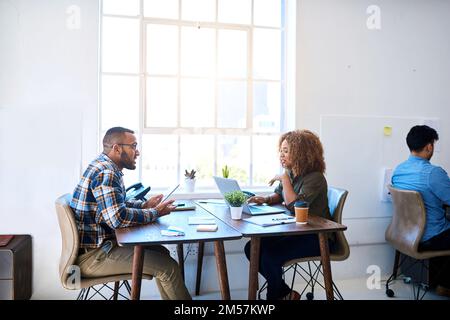 Open plan promotes open discussions. two young coworkers having a discussion opposite each other in a modern office. Stock Photo