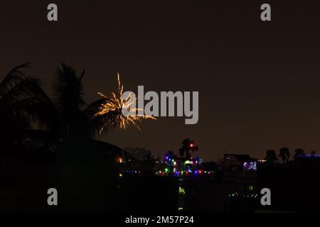 firework during celebration of new year, diwali and other festivals. shot taken against night sky with colorful lights in distant houses. Stock Photo