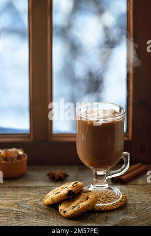 hot chocolate or cocoa with marshmallows in glass cup on table with winter window Stock Photo