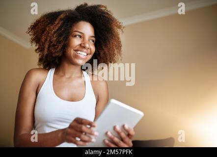 With wireless technology she doesnt miss a thing. a young woman using a digital tablet at home in the morning. Stock Photo