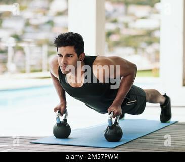 Pushing himself a little further every day. a young man doing pushups with dumbbells at home. Stock Photo