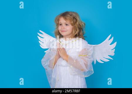 Kid wearing angel costume white dress and feather wings with prayer hands, hope and pray concept. Innocent child. Stock Photo