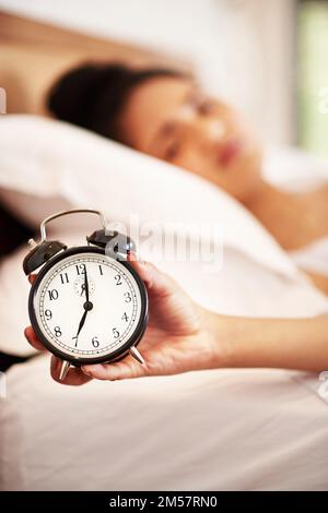Get a bright and early start to your day. Portrait of a young woman holding an alarm clock while waking up from bed in the morning. Stock Photo